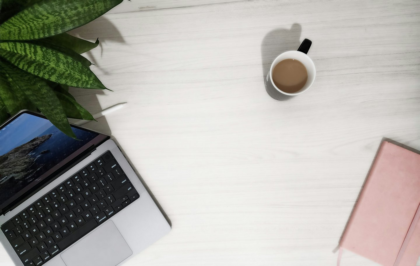 Laptop, coffee, notebook, and plant on a wooden desk.
